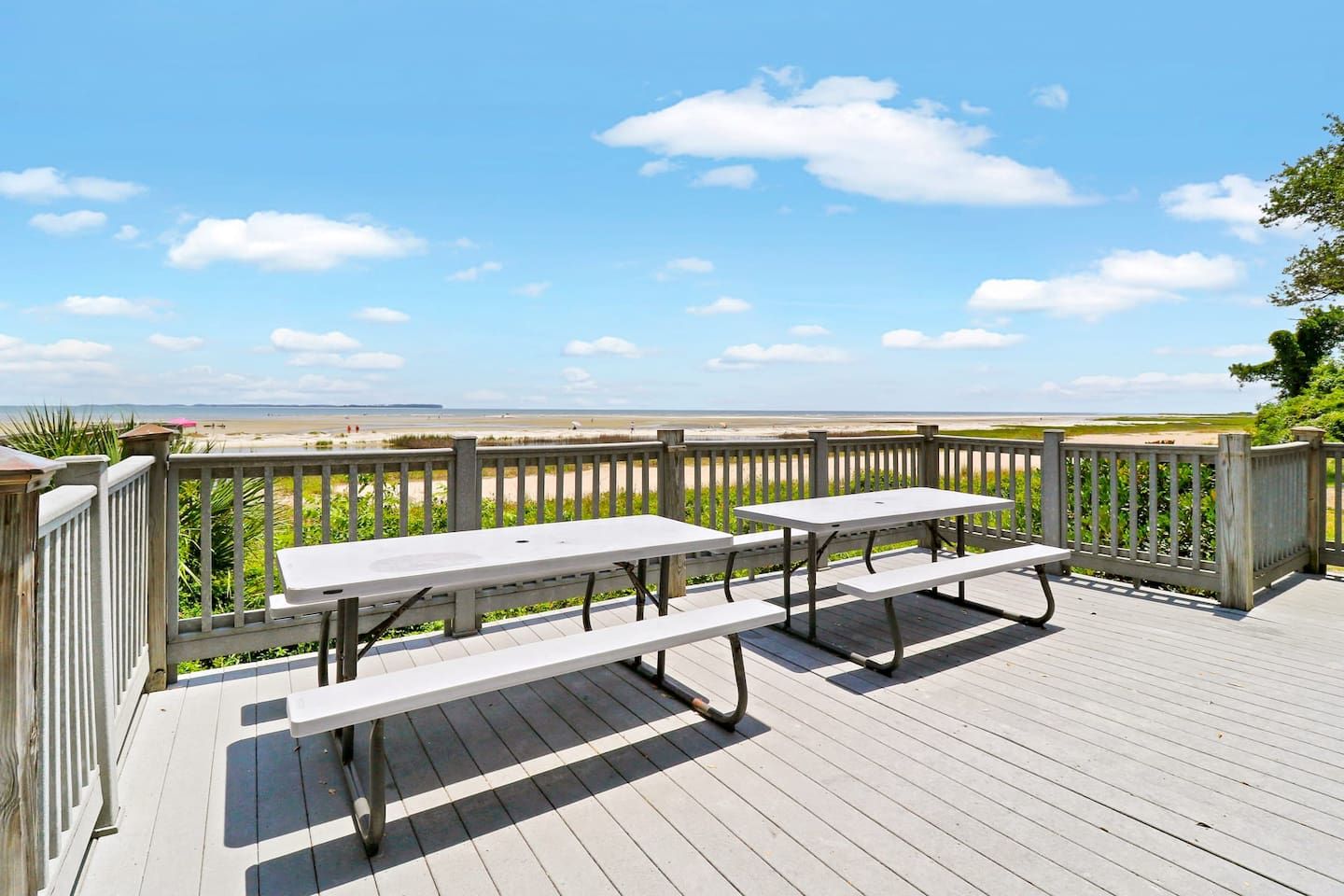A wooden deck with picnic tables overlooking a beach.