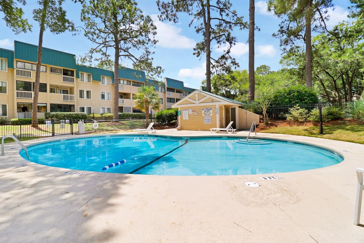 A pool area with a lifeguard station, lounge chairs, and a building with multiple balconies in the background.