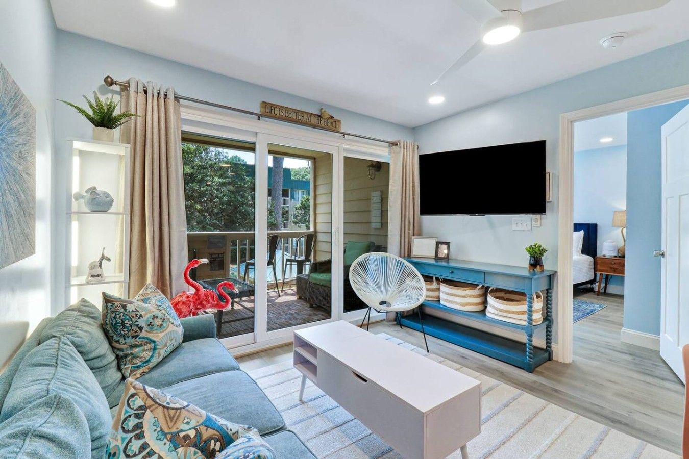 Un salon comprenant un canapé, une table basse, un téléviseur et un balcon donnant sur une piscine.