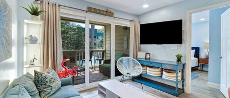 Un salon comprenant un canapé, une table basse, un téléviseur et un balcon donnant sur une piscine.