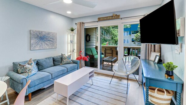Een moderne woonkamer met een bank, een salontafel, een televisie en een balkon met buitenmeubilair.