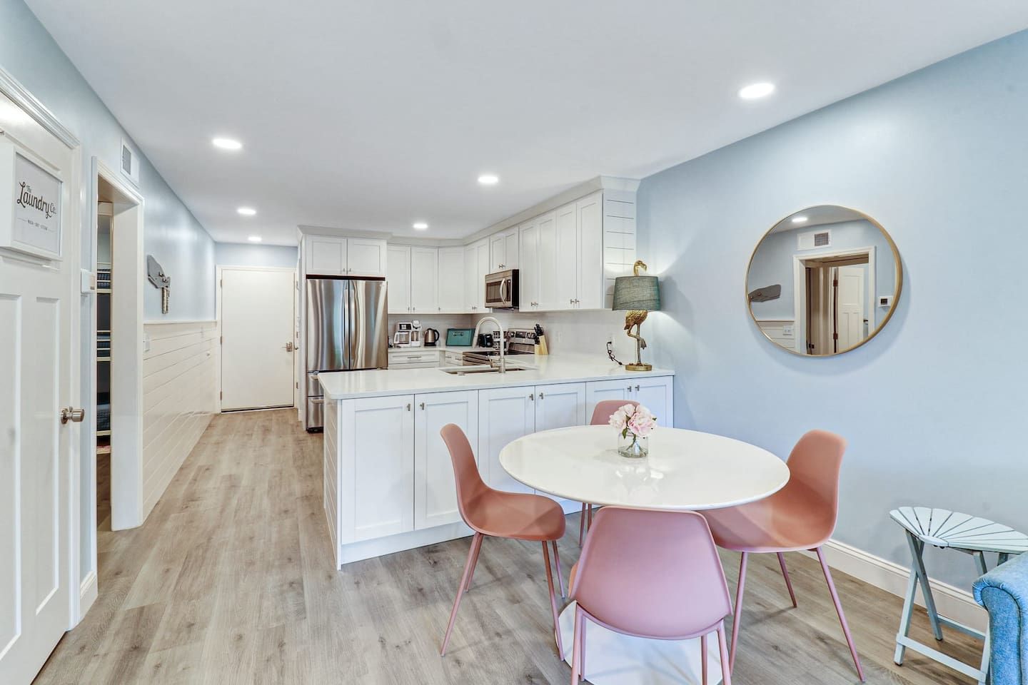 A modern kitchen with white cabinetry, stainless steel appliances, and a central island with pink chairs.