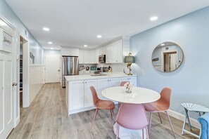 A modern kitchen with white cabinetry, stainless steel appliances, and a central island with pink chairs. - Stunning 2 Bedroom Villa Steps to the Beach (Hilton Head Island)