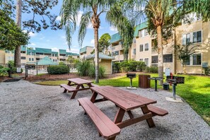 A courtyard with picnic tables, a barbecue grill, and a trash can. - Stunning 2 Bedroom Villa Steps to the Beach (Hilton Head Island)