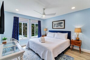 A bedroom with a bed, a ceiling fan, a window with curtains, a bedside table with a lamp, and a framed picture on the wall. - Stunning 2 Bedroom Villa Steps to the Beach (Hilton Head Island)