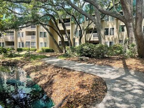A residential building with multiple balconies, a paved pathway, and a small pond. - Stunning 2 Bedroom Villa Steps to the Beach (Hilton Head Island)