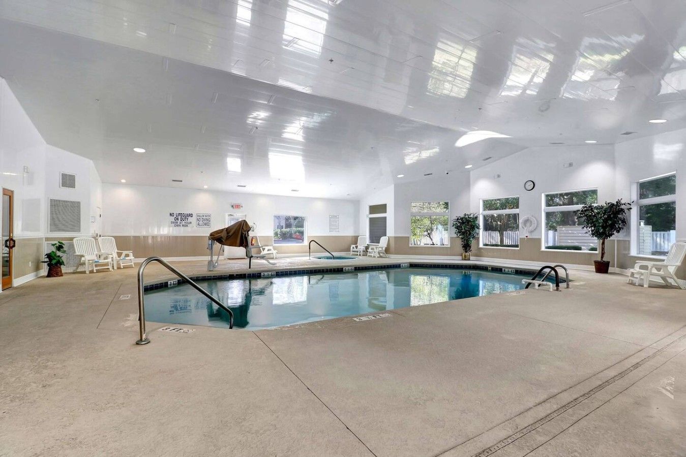 Une piscine intérieure à l’eau claire, entourée de chaises longues et de plantes en pot.