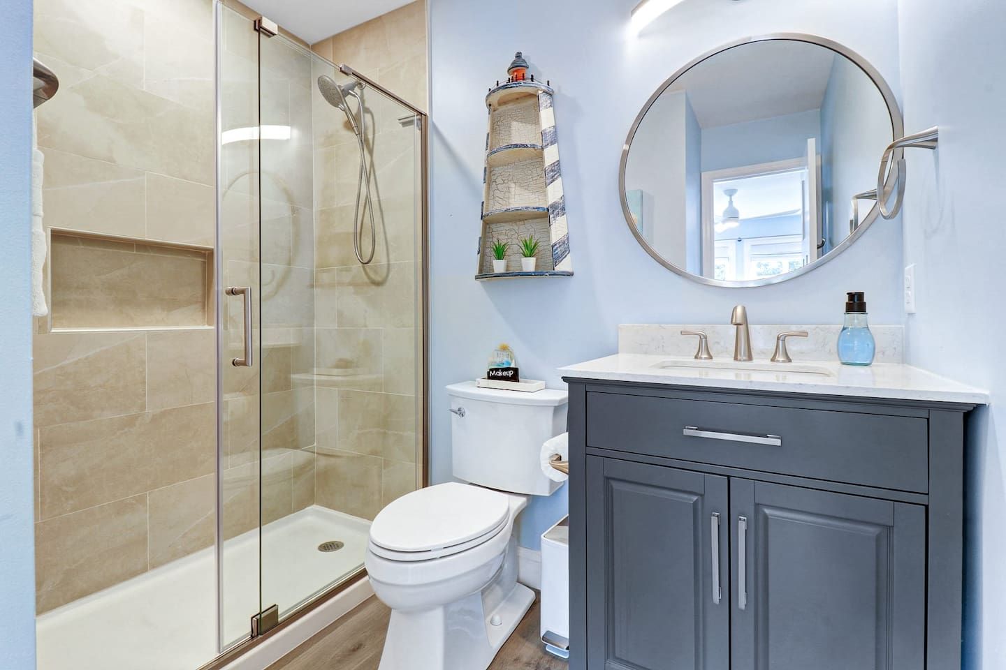 A modern bathroom with a glass-enclosed shower, a toilet, a vanity with a mirror, and a decorative lighthouse shelf.