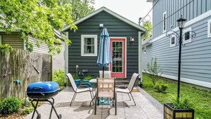 Eine Terrasse mit Grill, Gartenmöbeln und einem kleinen Schuppen mit roter Tür.