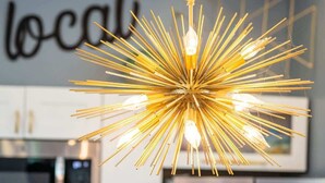 Eine moderne Küche mit Edelstahlgeräten, einer hängenden, goldfarbenen Sternleuchte und einer Wand, auf der ein Wort teilweise sichtbar ist.