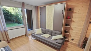 Un soggiorno moderno con un divano grigio, scaffali in legno e una grande finestra che si affaccia sul verde.
