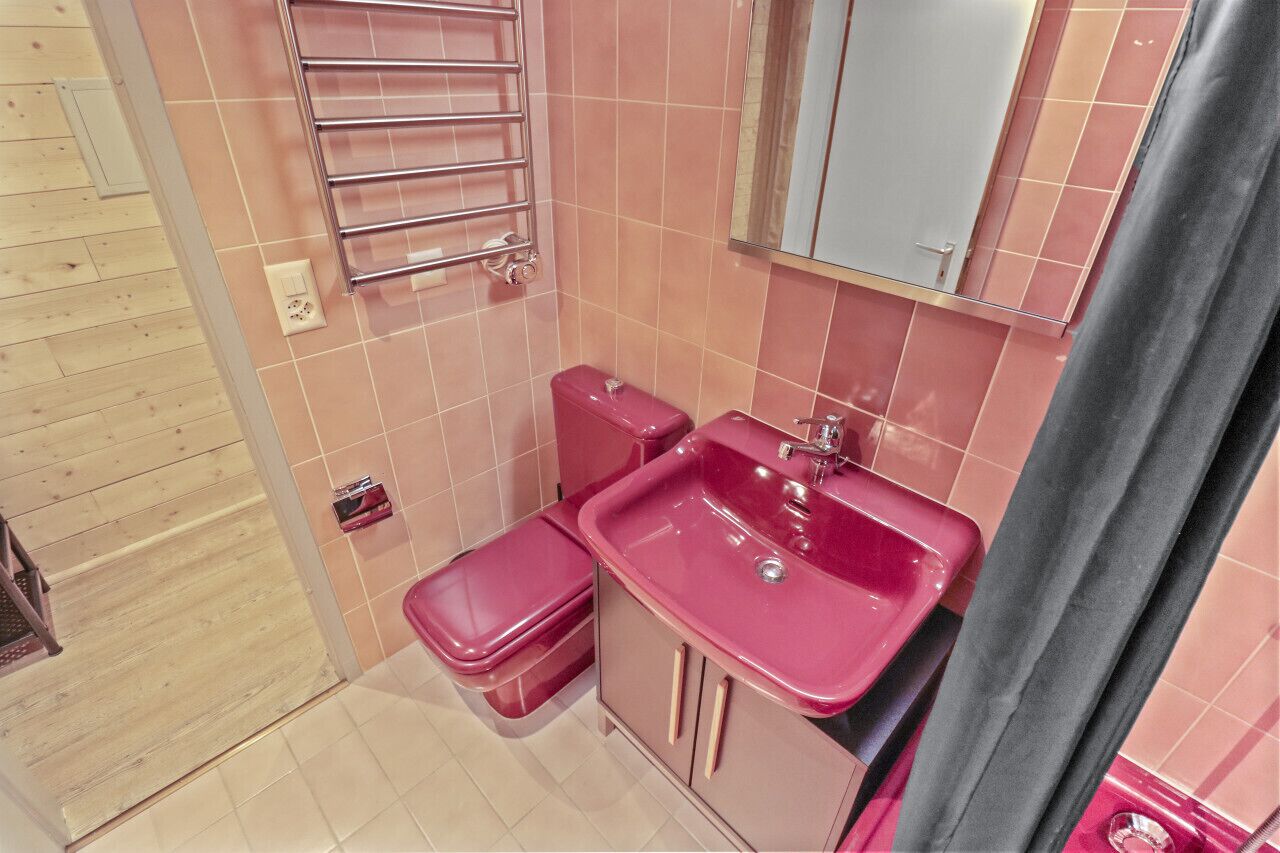 Une petite salle de bain avec des carreaux roses, un lavabo, des toilettes et un porte-serviettes.