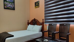 Un dormitorio con una cama, dos sillas de madera, una mesita y un cuadro en la pared.