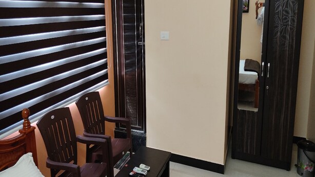 Una habitación con un sofá, dos sillas de madera, una mesa de centro con controles remotos, una puerta con un espejo y un cubo de basura.