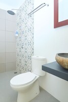 Un baño con inodoro, ducha y lavabo con cuenca de piedra.