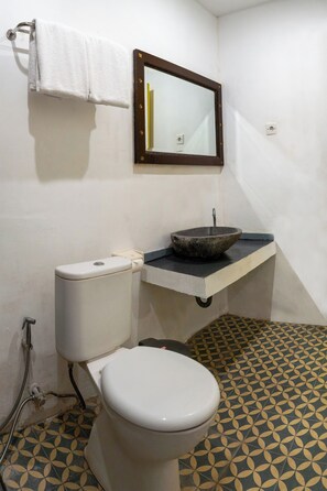 A bathroom with a toilet, a sink with a stone basin, a mirror, and patterned floor tiles. - Attara Inn Senggigi (Senggigi)