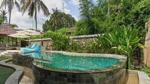 A curved swimming pool with a stone border, surrounded by lush greenery and a stone wall. - Attara Inn Senggigi (Senggigi)