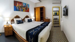 A bedroom with a large bed, a wooden wardrobe, a small bedside table, a TV mounted on the wall, and a bathroom with a sink and mirror. - Attara Inn Senggigi (Senggigi)