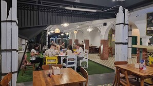 An indoor dining area with wooden tables and chairs, a green carpet, and a brick column. - Attara Inn Senggigi (Senggigi)