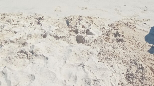 En strand med kristallklart, turkosfärgat vatten och fotspår i sanden.