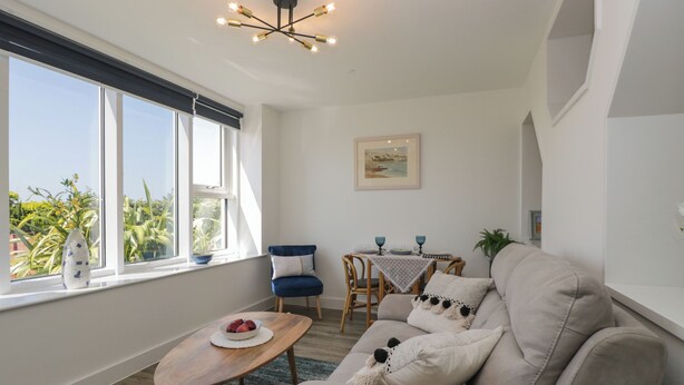 A living room with a sofa, a wooden coffee table, a blue chair, a dining table with blue glassware, and a painting on the wall. - The Studio (Weston-super-Mare)
