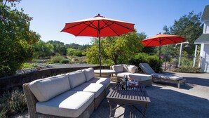 A patio area with wicker furniture, including a sofa and chairs, under two red umbrellas. - Country chic cottage and connected water tower next to Jordan winery (Healdsburg)