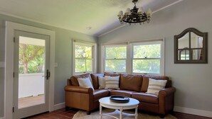 A room with a brown leather sofa, a white coffee table, and a large window with a view of trees. - Country chic cottage and connected water tower next to Jordan winery (Healdsburg)