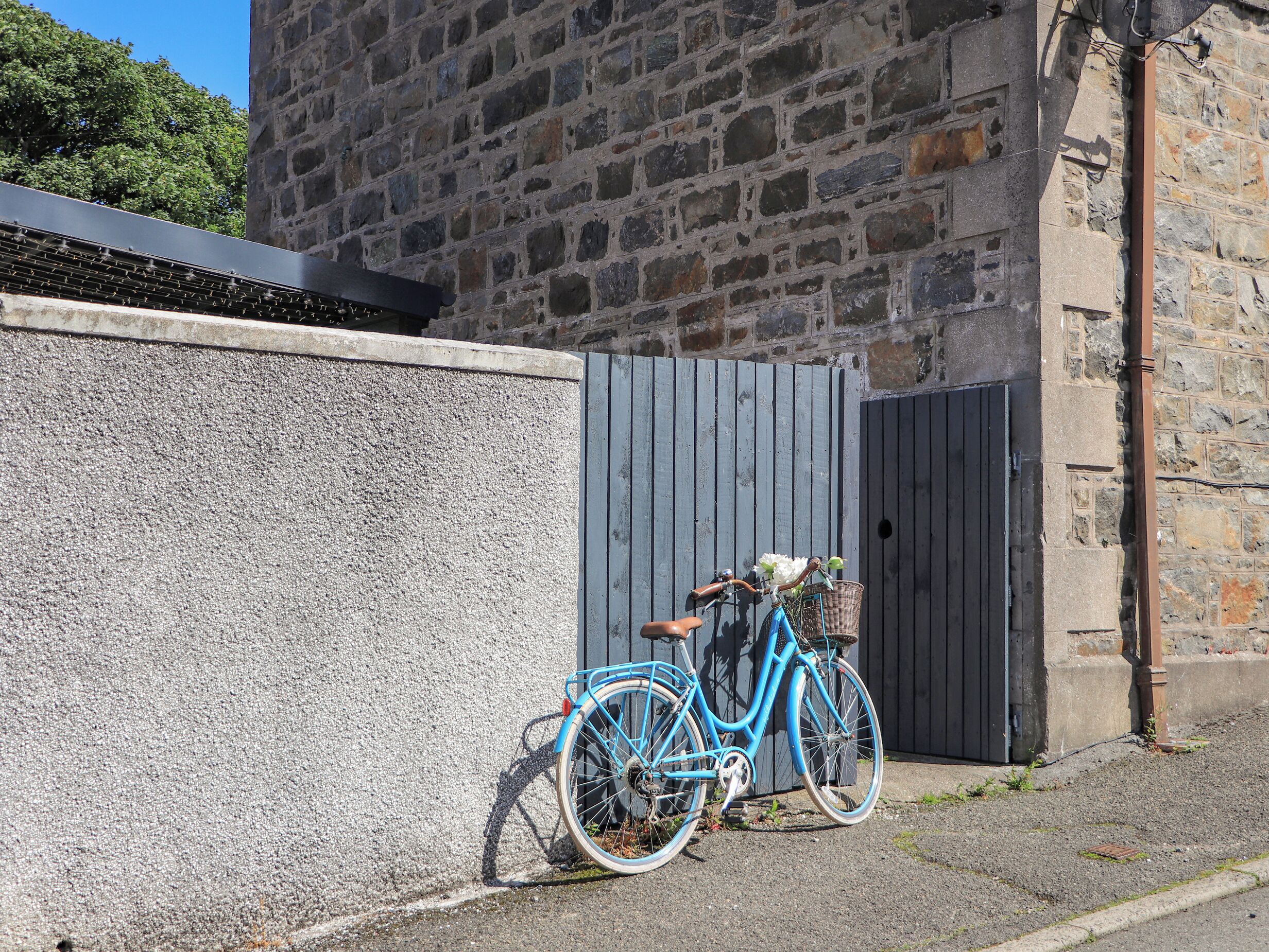 A blue bicycle parked against a stone wall with a wooden door in the background.