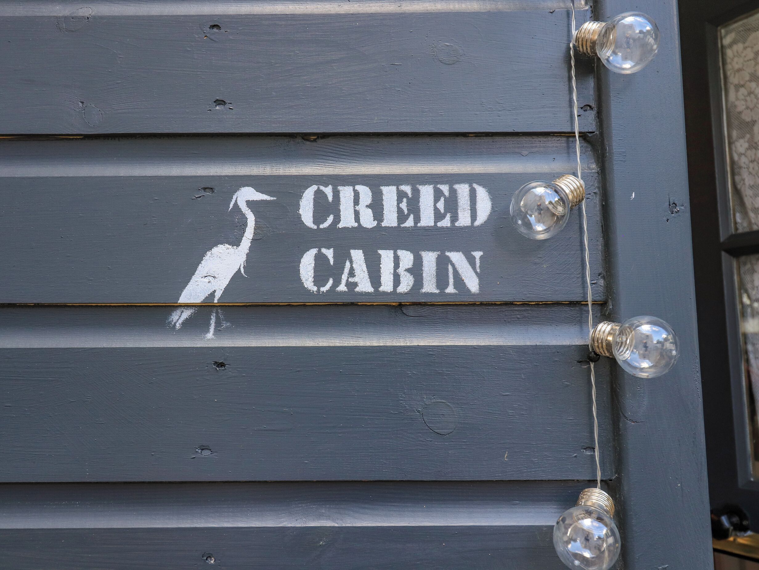 A wooden sign with the text "CREED CABIN" and a bird silhouette.