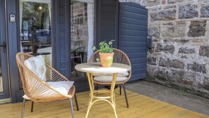 Een terras met rieten stoelen en een tafel, een bloempot en een stenen muur.
