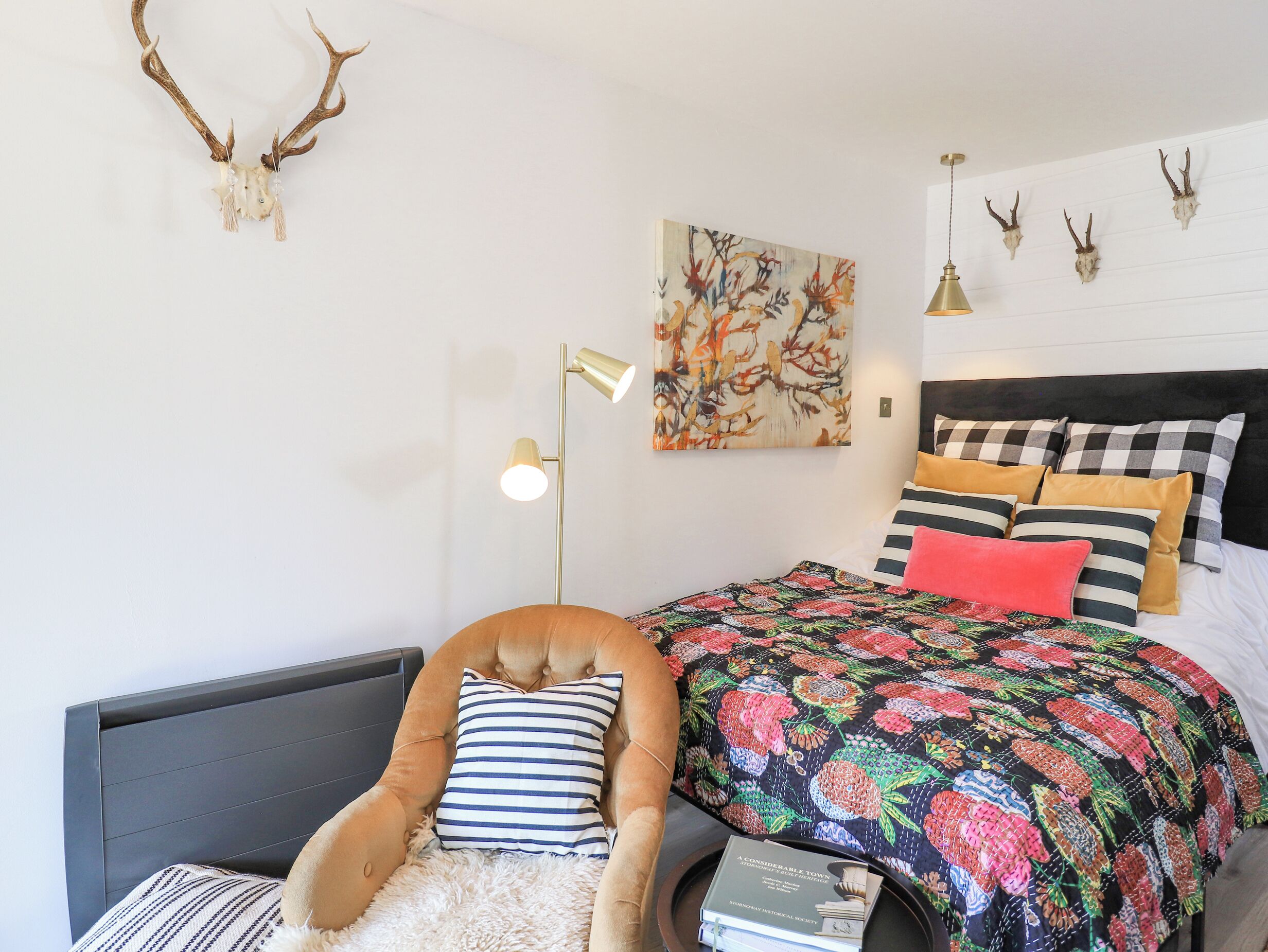Ein Schlafzimmer mit einem Bett, einem Sessel, einer Stehlampe und Wandleuchtern in Form von Hirschgeweihen.