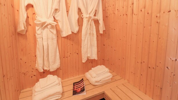 Een sauna met houten wanden, twee handdoeken aan haakjes en een opgevouwen handdoek op de vloer.