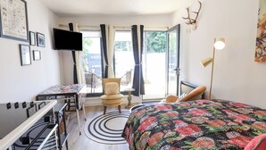 Een slaapkamer met een bed, een bureau, een stoel en een tafel. Er is een raam met gordijnen, een aan de muur bevestigde televisie en een lamp.