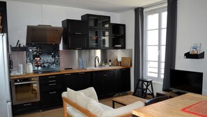 Eine moderne Küche mit schwarzen Schränken, einer Holzarbeitsplatte und einem eingebauten Ofen. Es gibt ein weißes Sofa und einen Esstisch mit Stühlen.