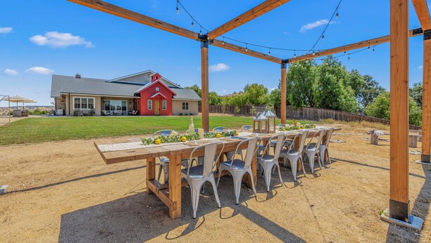 An outdoor patio with a wooden pergola, string lights, and a table set for dining.