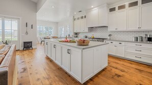A spacious kitchen with white cabinetry, a large island, and wooden flooring.