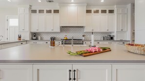 A modern kitchen with white cabinetry, a central island, and a stainless steel range hood.