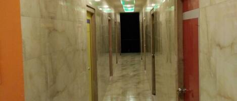 Un pasillo con suelo de mármol, iluminación verde tenue y puertas a ambos lados, que termina en la oscuridad.