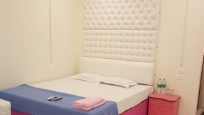 A bedroom with a bed, a bedside table, an air conditioning unit, and a bathroom door. - Hotel Royal Palace (Port Blair)