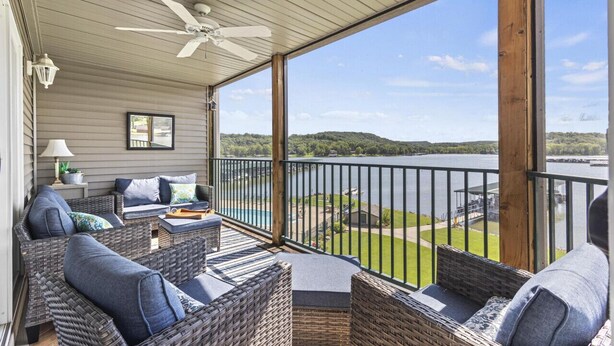 A covered balcony with wicker furniture, a ceiling fan, and a view of a lake and hills.