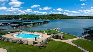 A swimming pool with lounge chairs and a small building, surrounded by a grassy area and a dock with boats.