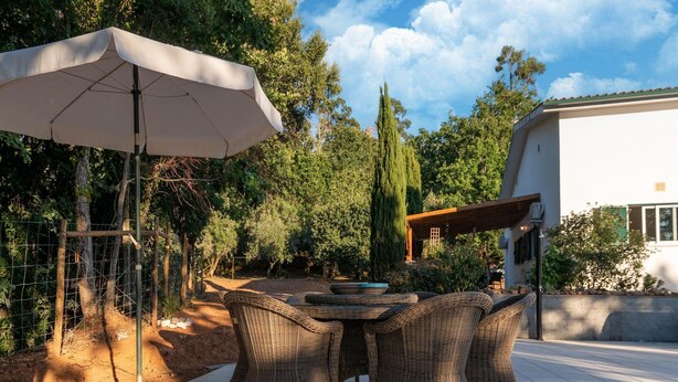 An outdoor patio with wicker furniture, a table, and a large umbrella. - Comfy house with large garden and swimming pool (Folques)