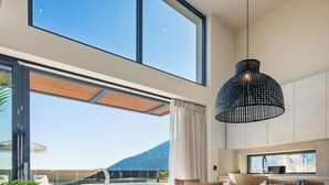 Uma cozinha moderna com uma janela ampla, uma luminária pendente e vista para uma piscina e montanhas.