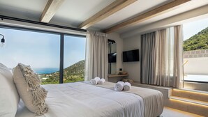 Quarto com cama grande, vista para o mar e teto de madeira.