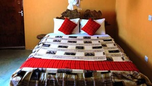 Un lit avec une couvre-lit à motifs, deux oreillers rouges et un baldaquin blanc.