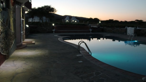 Une piscine avec une terrasse en pierre et un bâtiment dont la façade est également en pierre, visible au fond.
