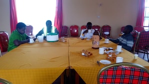 Une salle de conférence avec une longue table, des chaises à carreaux rouges et divers objets disposés sur la table, notamment des tasses, un thermos et un microphone.
