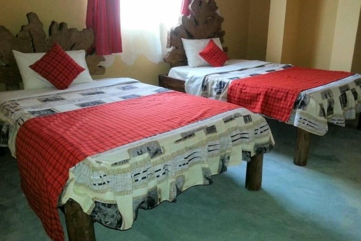Two single beds with red and white checkered bedspreads, wooden headboards, and red curtains.
