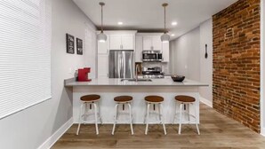 Cozinha moderna com armários brancos, eletrodomésticos de aço inoxidável e uma parede de tijolos.