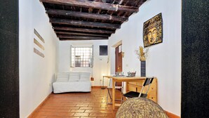 A small, cozy room with a bed, a desk, and a chair. There is a window with a view of the outside, a door, and a wall with a decorative piece. - Luxury Maison Colosseum, like a resident (Roma)